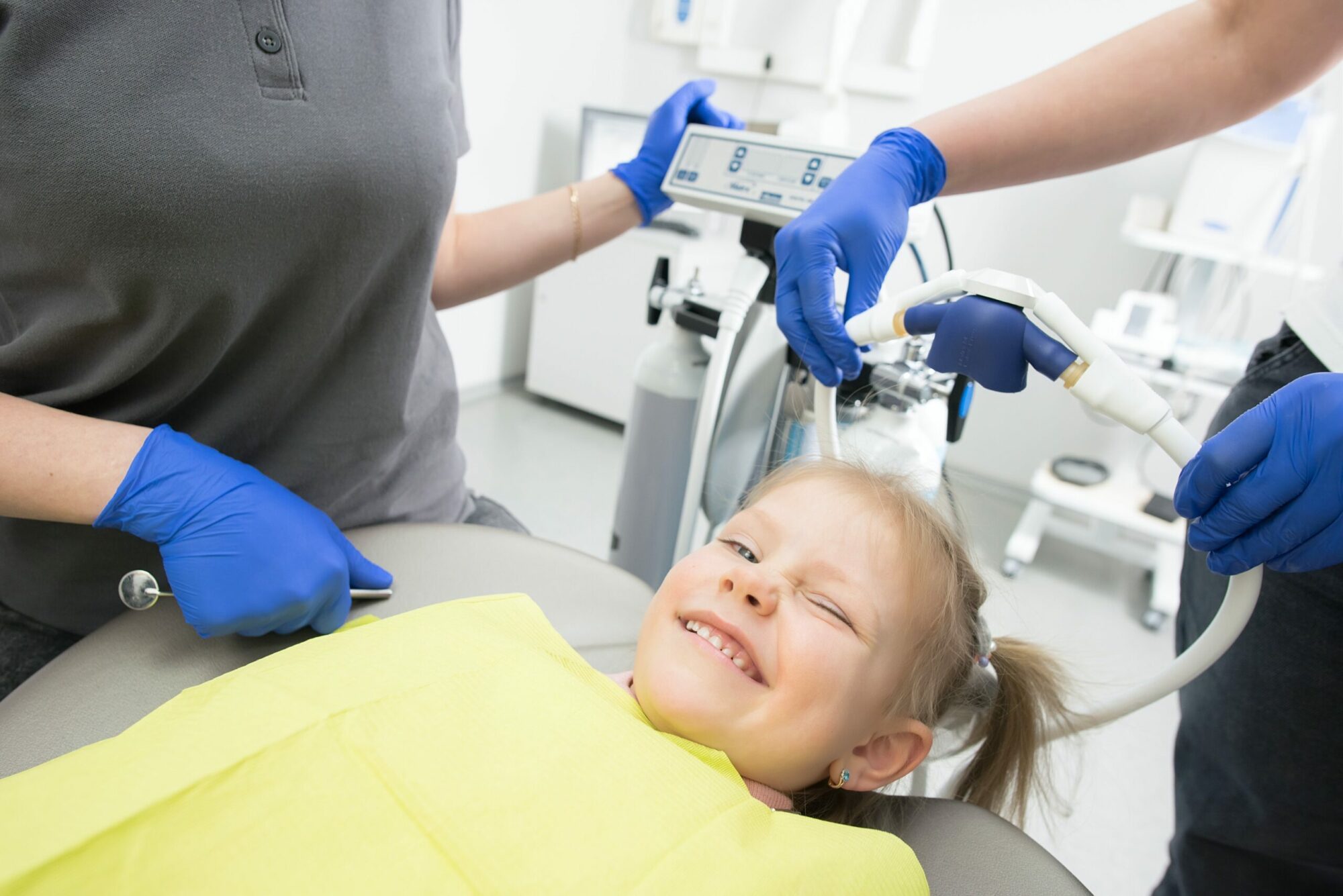 A blond child in a dentist's chair, smiling at the camera