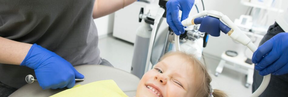 A blond child in a dentist's chair, smiling at the camera