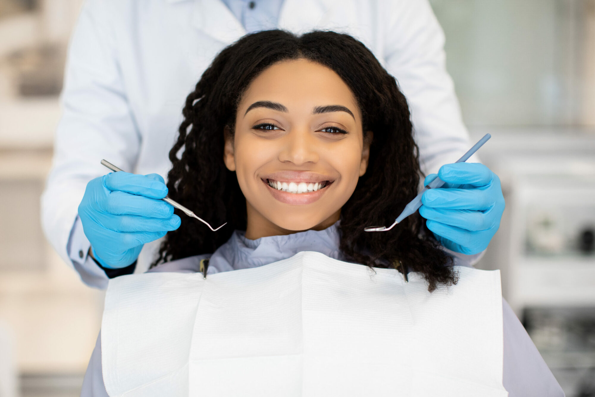 Portrait Of Happy Young Black Woman Having Check Up At Dental Clinic, Closeup Shot Of Millennial African American Female Patient Getting Teeth Treatment With Dentist In Modern Stomatologic Cabinet