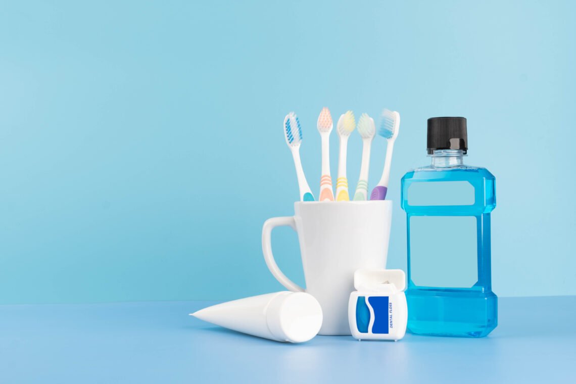 Oral care products set for healthy teeth and gums. Toothbrushes in glass with toothpaste, mouthwash and dental floss on blue background. Copy space.