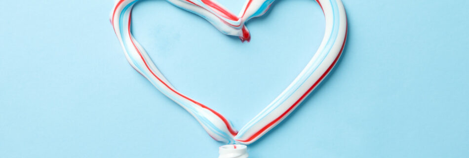 Heart made of toothpaste and tube on blue background, top view