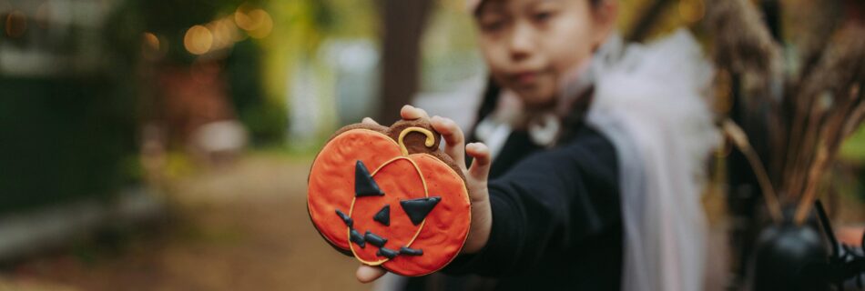 A kid n Halloween holding up a pumpkin cookie meant to discourage kids from eating too much sugar on halloween