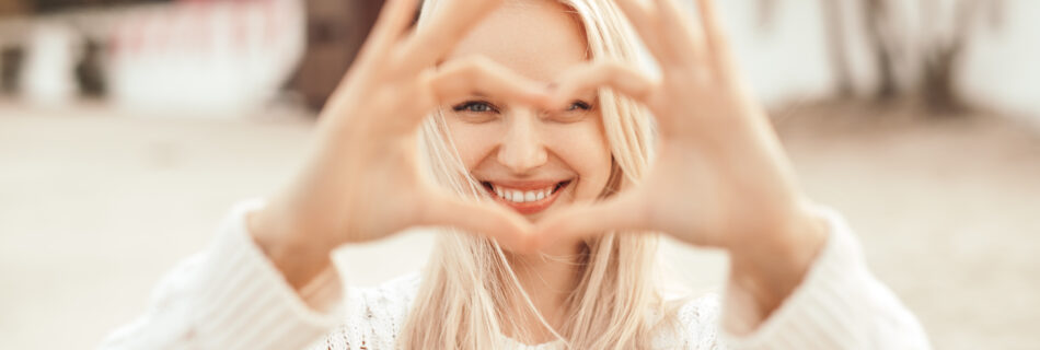 Woman smiling, holding her hands up to form a heart shape in front of her face.