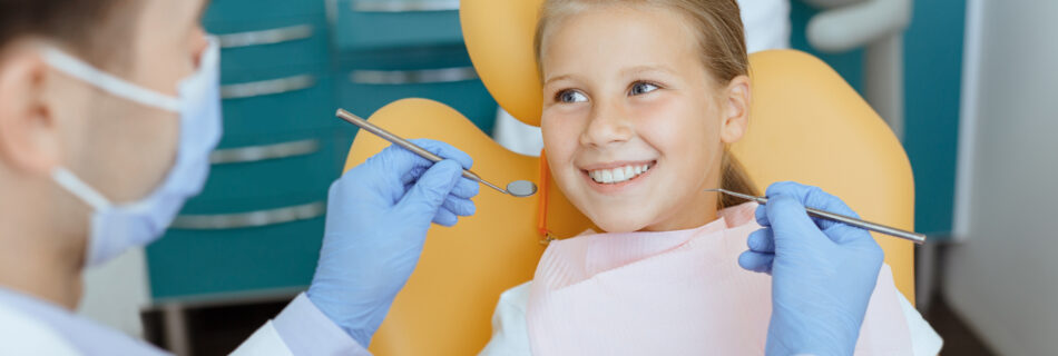 A young girl smiles in a dentist chair during her appointment.